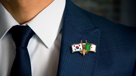 Empresario-caminando-hacia-cámara-con-amigo-país-banderas-Pin-Corea-del-sur---Argelia