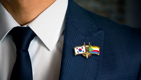 Empresario-caminando-hacia-cámara-con-amigo-país-banderas-Pin-Corea-del-sur---Comoras