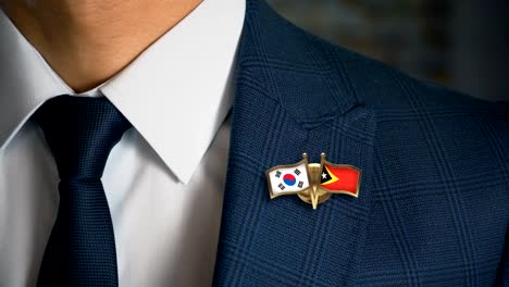 Geschäftsmann-zu-Fuß-in-Richtung-Kamera-mit-Freund-Land-Flaggen-Pin-Südkorea---Ost-Timor