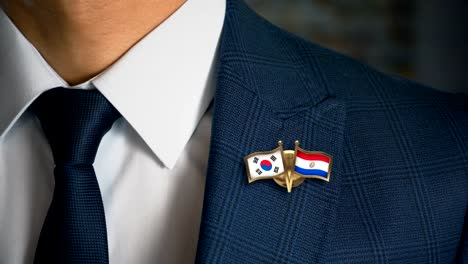 Geschäftsmann-zu-Fuß-in-Richtung-Kamera-mit-Freund-Land-Flaggen-Pin-Südkorea---Paraguay