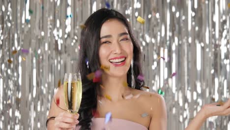 Schöne-asiatische-Frau-mit-Glas-Champagner-tanzen-unter-Konfetti-über-Silber-Glitzer-Hintergrund,-Slow-motion