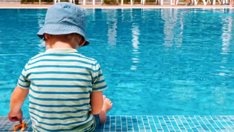 Happy-little-boy-sitting-near-the-pool