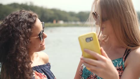 Zwei-fröhliche-Mädchen-Selfies-an-einem-See-machen.