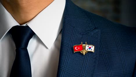 Empresario-caminando-hacia-cámara-con-amigo-país-banderas-Pin-Turquía---Corea-del-sur