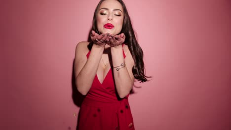 Brunette-happy-woman-give-air-kiss-with-confetti-in-pink-background-wear-red-dress