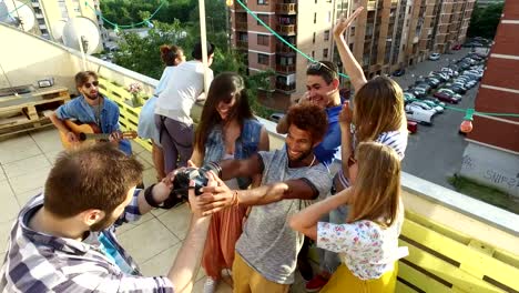 Happy-people-taking-photos-and-laughing-at-the-rooftop,-musician-playing-guitar