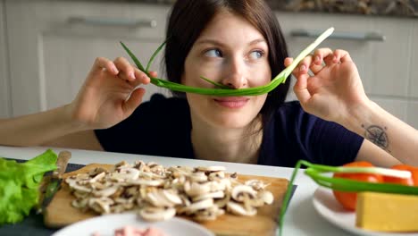 schöne-lustige-Frau-Koch-spielen-mit-grüner-Zwiebel-auf-dem-Tisch-in-der-Küche-zu-Hause