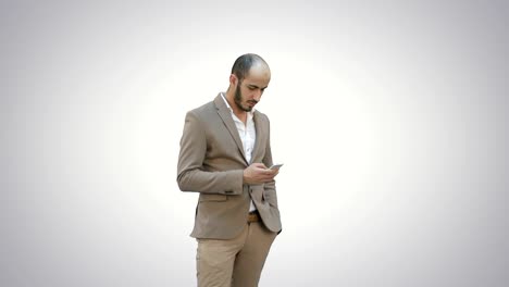 Young-man-in-suit-walking-and-sending-text-message-on-mobile-phone-on-white-background