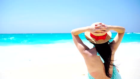 Back-view-of-beautiful-woman-in-hat-on-summer-holidays-on-white-beach.