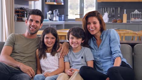 Portrait-Of-Smiling-Family-Sitting-On-Sofa-In-Lounge-Together