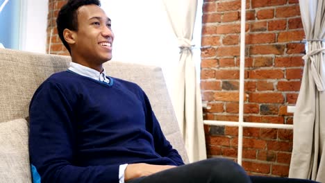 Smiling-Young-African-Man-Sitting-with-Loft-Background