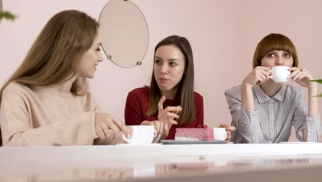 Three-young-Caucasian-girls-sitting-in-a-cafe,-drinking-coffee,-eating-cake,-smiling,-laughing,-gesturing-with-their-hands,-gossip-old-girlfriends-in-a-cafe-concept.-60-fps