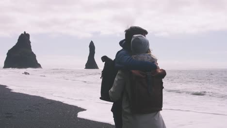 Junges-paar-umarmt-und-Enjoing-Blick-auf-schwarzen-Sandstrand-in-Island,-Slow-motion