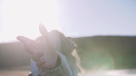 Young-woman-with-leather-bagpack-rising-hands-enjoying-view-near-the-coastal-landscape-in-Iceland,-cinematic-shot,-rack-focus