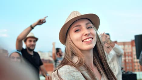 Beautiful-European-woman-in-hat-taking-selfie-using-camera-or-smartphone-at-summer-rooftop-party