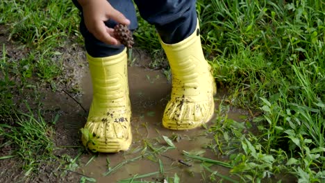 Kleines-Kind-in-leuchtend-gelben-Latex-Stiefel-in-einer-Pfütze-planschen.-Kid-es-Füße-geschützt-von-Schmutzwasser