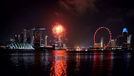 Fireworks-of-Singapore-National-Day-in-Downtown-Singapore-city-in-Marina-Bay-area-at-night.-Financial-district,-The-Ferris-Wheel,-and-skyscraper-buildings.