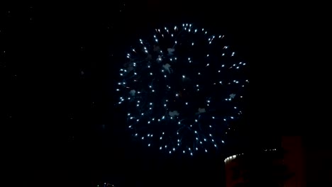 Fuegos-artificiales-sobre-la-ciudad.-Hermosos-destellos-azules-explotan-en-el-cielo-nocturno-sobre-el-fondo-de-los-edificios.-Espectáculo-de-fuegos-artificiales.