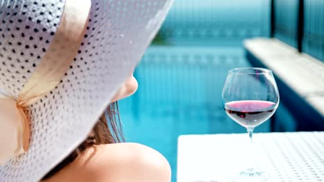 Portrait-smiling-pretty-woman-in-floppy-hat-and-sunglasses-enjoying-sunbathing-with-goblet-of-wine