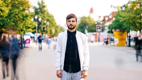 Time-lapse-retrato-de-hombre-joven-serio-mirando-a-pie-de-cámara-en-el-centro-de-la-calle-peatonal-muy-transitada-en-verano-usa-ropa-elegante-mientras-que-las-personas-pasan.