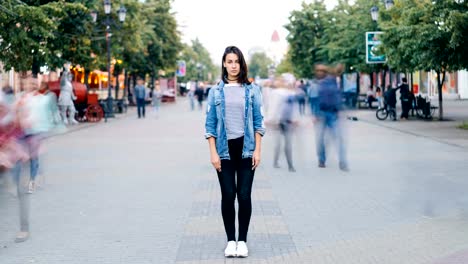 Time-Lapse-Porträt-der-gestresste-junge-Frau-allein-im-Zentrum-der-Stadt-trägt-Jeans-und-Jeansjacke-und-Blick-in-die-Kamera,-während-Menschen-vorbeifahren.