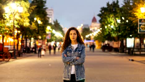 Zeitraffer-der-gut-aussehende-Frau-Towny-in-Jeans-Kleidung-für-sich-allein-auf-der-Straße-unter-den-Massen-von-Menschen-und-Blick-in-die-Kamera.-Straßenlaternen-sind-sichtbar.