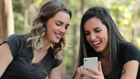 Authentic-friends-together-outdoors-checking-cellphone.-Girls-looking-and-holding-smartphone-chatting-exchanging-gossip