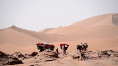 Una-pequeña-caravana-de-camellos-y-beduins-caminando-sobre-las-llanuras-appoaching-las-dunas-de-arena
