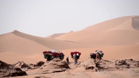 Eine-kleine-caravan-Kamelen-und-beduins-Fuß-auf-die-Prärie-appoaching-den-sand-dunes