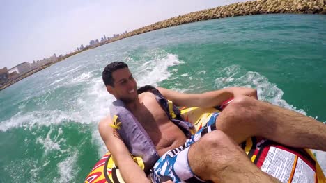 Man-sitting-in-inflatable-ring-towed-by-a-boat-in-the-water-and-recording-himself-with-Go-Pro-camera