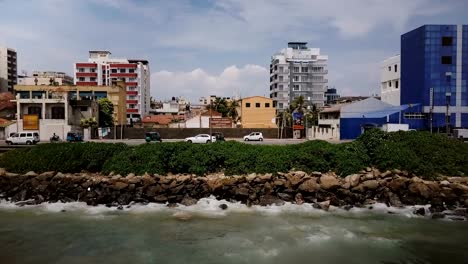 Drohne-fliegen-entlang-Ozean-Küste-in-Colombo,-Sri-Lanka-Straße-links.-Tracking-Luftaufnahme-von-asiatischen-Resort-Stadt-Meeresküste