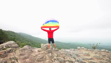 man-raise-rainbow-colour-LGBTI-flag-waving-in-hard-wind-on-mountain-top-viewpoint