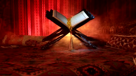 Open-holy-book-of-Muslims-on-stand-on-eastern-carpet-with-dark-toned-foggy-background.-Muslim-religion-concept.-Selective-focus.-Slider-shot.