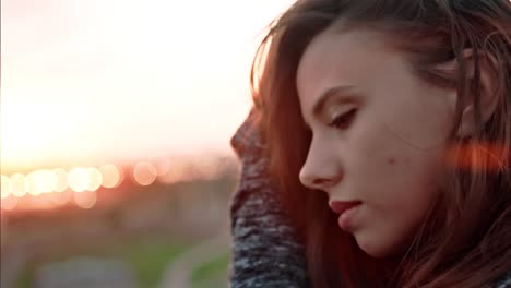 Close-up-face-of-young-pensive-woman-melancholically-looking-at-amazing-sunset-and-touching-hair