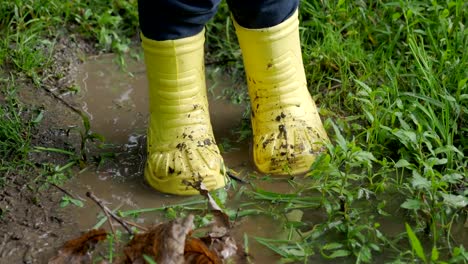 Niño-pequeño-en-goma-amarilla-brillante-botas-chapoteando-en-un-charco.-Pies-de-niño-protegidos-de-agua-sucia