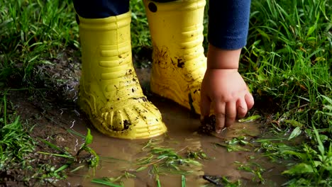 Niño-pequeño-en-goma-amarilla-brillante-botas-chapoteando-en-un-charco.-Pies-de-niño-protegidos-de-agua-sucia