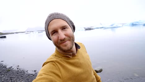 Young-man-taking-selfie-with-glacier-lake,-icebergs-floating-on-water-in-Iceland