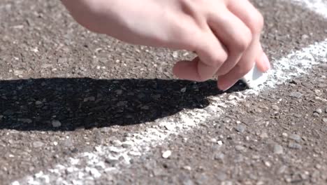 Frau-zieht-eine-Linie-auf-dem-Asphalt-mit-weißer-Kreide.-Close-up-Hand.