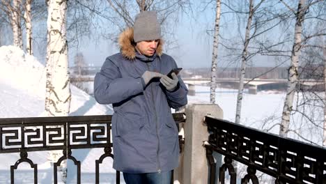 Hombre-de-chaqueta-azul-con-capucha-de-piel-limpia-la-pantalla-del-teléfono-con-la-mano-en-guantes-en-invierno.