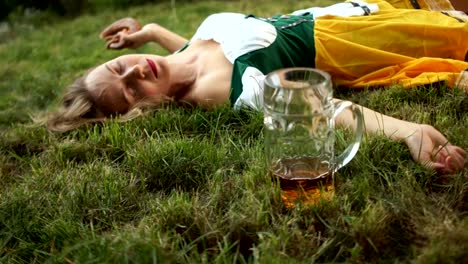 Asocial-behavior,-excessive-drinking.-A-woman-in-a-national-Bavarian-costume-lies-on-the-grass-next-to-an-empty-beer-glass.-Close-up.-Festival-Oktoberfest