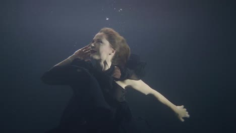 Mysterious-woman-in-black-dress-swimming-like-mermaid-under-water-in-dark-pool