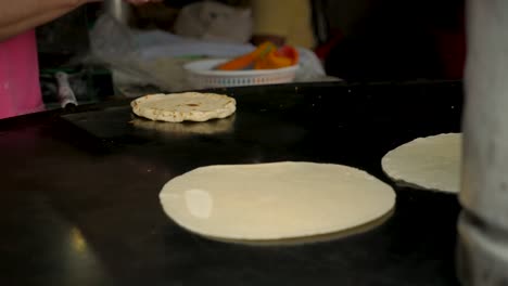 Cerca-de-la-mano-de-una-mujer-los-bancos-una-tortilla-de-maíz-hecha-a-mano-en-una-bandeja-de-metal