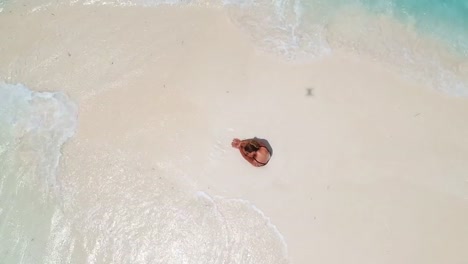 Wunderschöne-Frau-sonnt-sich-auf-Sand-Zunge-umgeben-von-türkisblauem-Wasser