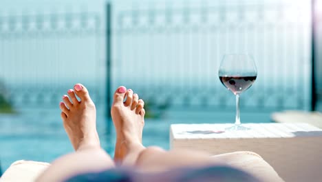 POV-shot-woman-relaxing-having-sunbath-lying-on-deck-chair-playing-bare-feet-with-bocal-of-red-wine