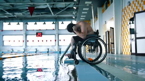 Disabled-man-in-a-wheelchair-putting-on-a-swimming-cap-and-a-goggles.-Side-angle