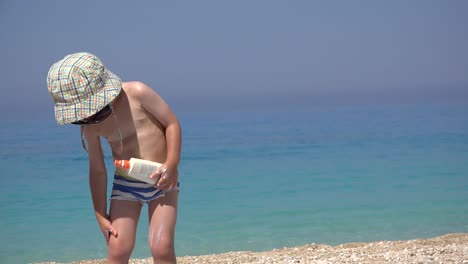 Funny-little-child-with-sunglasses-and-hat-applying-sun-cream-on-his-body