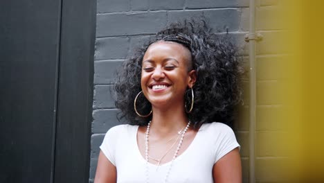 Fashionable-young-black-woman-relaxing-in-the-street-leaning-against-a-wall,-head-and-shoulders