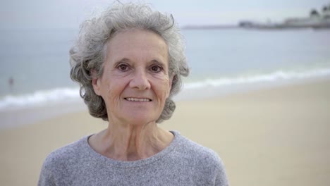 Happy-beautiful-elderly-woman-with-toothy-smile-posing-against-blurred-seascape-background.