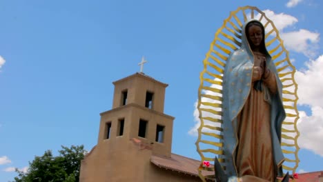 Panning-shot-of-a-Statue-of-Our-Lady-of-Guadalupe-in-front-of-an-Adobe-Church