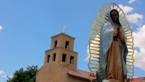 Panning-Shot-eine-Statue-der-Muttergottes-von-Guadalupe-vor-einer-Adobe-Kirche